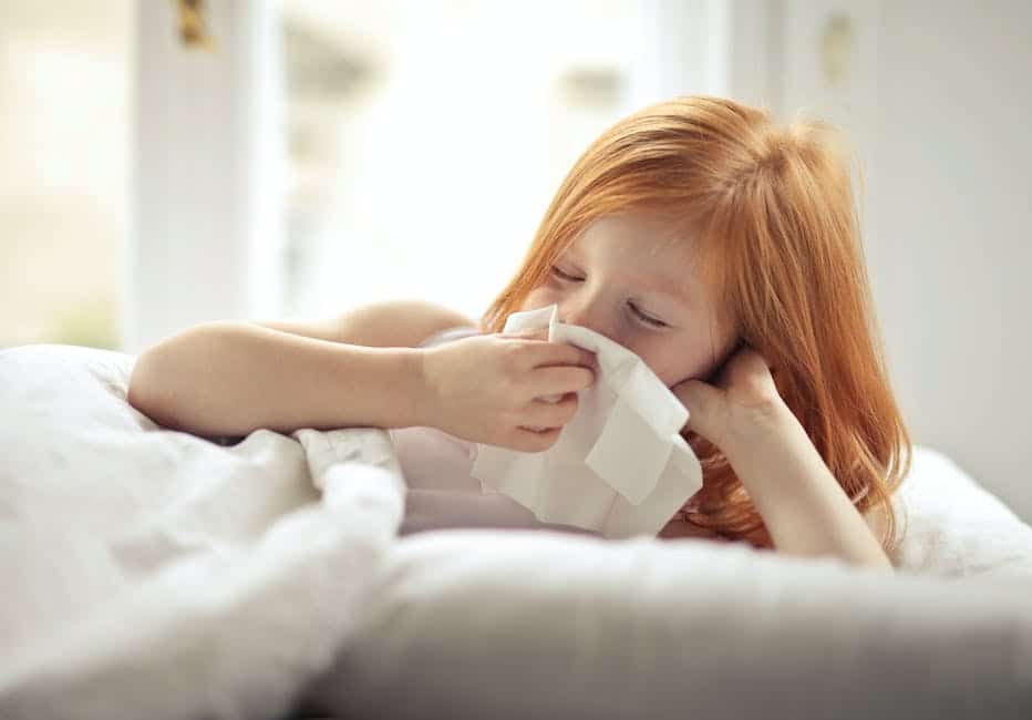 A person sneezing while holding a tissue and a dog sitting beside them.