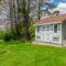 A gray shed contains white trim, two windows, and a roof with tan shingles. The shed sits next to mature trees.