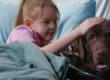 A large, relaxed brown dog laying in a hospital bed with a young girl. She is wearing a nasal cannula.
