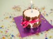 A birthday cake with an ignited candle sitting on top. There are brown dog bones surrounding the outer edge of the cake.