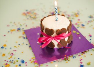 A birthday cake with an ignited candle sitting on top. There are brown dog bones surrounding the outer edge of the cake.