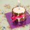 A birthday cake with an ignited candle sitting on top. There are brown dog bones surrounding the outer edge of the cake.